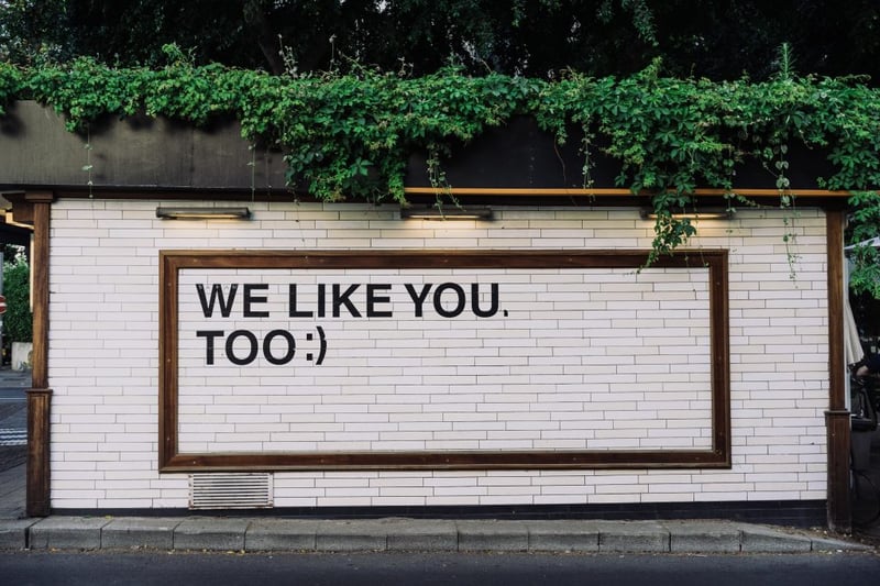 white brick wall with the slogan 'we like you too' and a smiley face behind it 